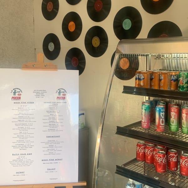 L.A. Waterfront Pizza menu board next to a beverage cooler with vinyl records decorating the wall.