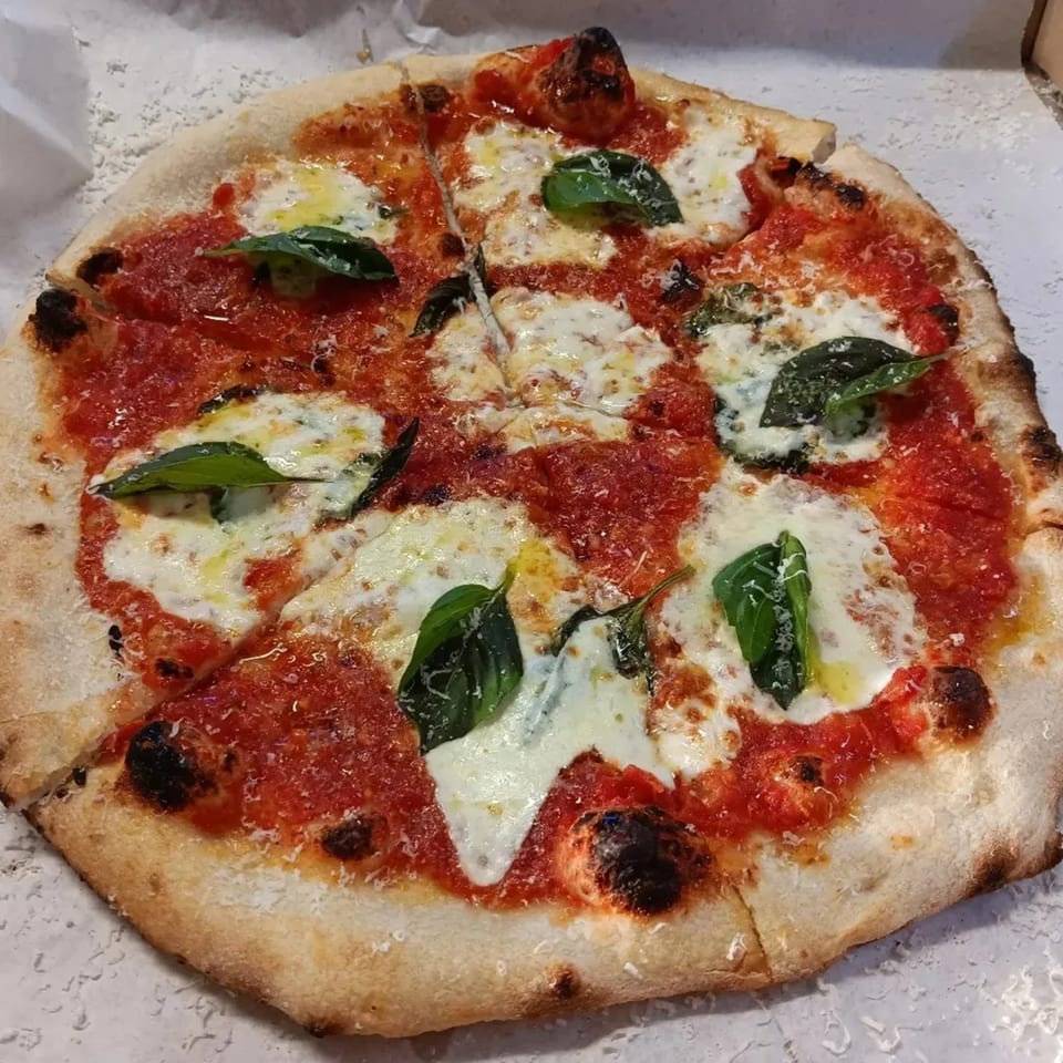 A freshly baked L.A. Waterfront Pizza Margherita, sliced, with vibrant red sauce, mozzarella, and basil.