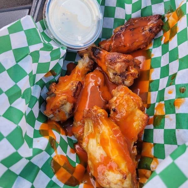 Buffalo chicken wings with sauce and a side of ranch dressing in a green and white checkered basket.
