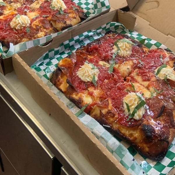 Two rectangular L.A. Waterfront pizzas with pepperoni, red sauce, cheese, and basil in takeout boxes.