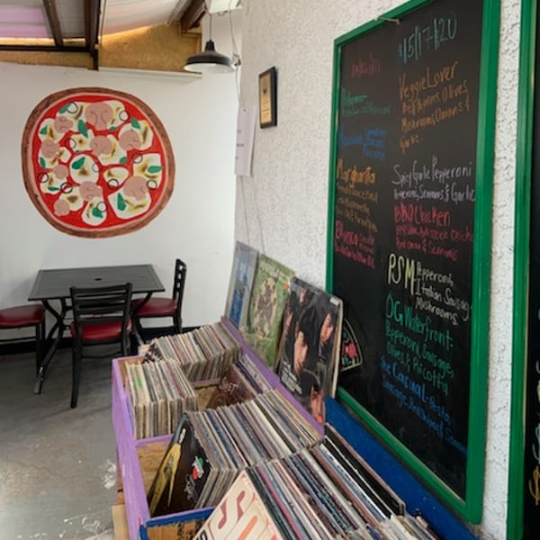 L.A. Waterfront Pizza interior with a pizza mural, menu chalkboard, and crates of vinyl records.