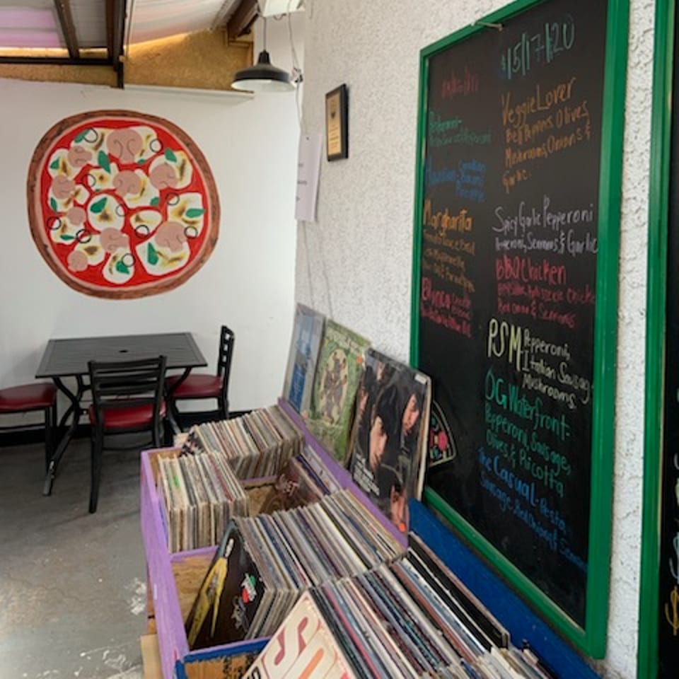 L.A. Waterfront Pizza interior with a pizza mural, menu chalkboard, and crates of vinyl records.