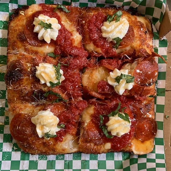 Square L.A. Waterfront Pizza with pepperoni, red sauce, dollops of cheese, and basil on checkered paper.