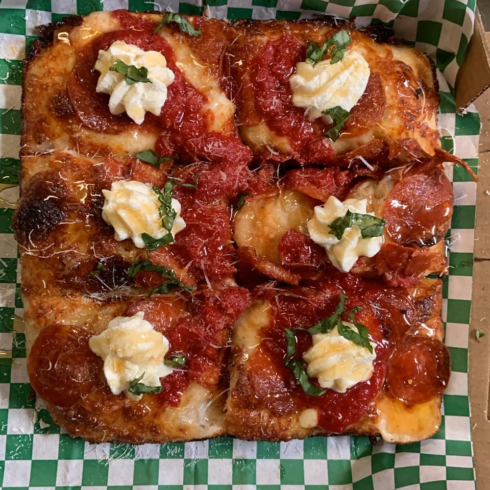 Square L.A. Waterfront Pizza with pepperoni, red sauce, dollops of cheese, and basil on checkered paper.