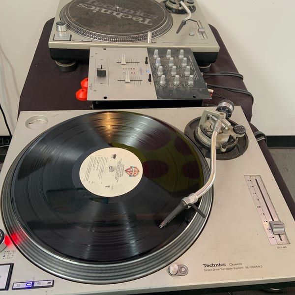 Two Technics turntables and a mixer set up for DJing, with a vinyl record playing.