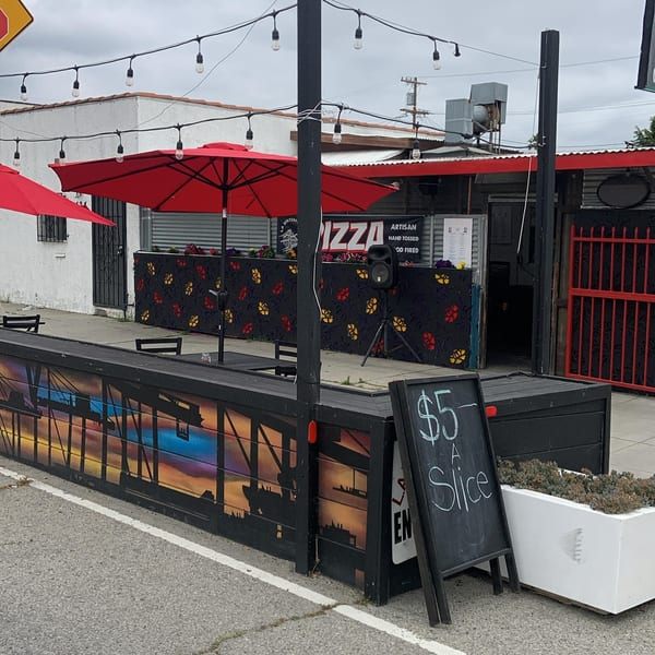 L.A. Waterfront Pizza's outdoor patio with red umbrellas, string lights, and a "$5 A Slice" sign.